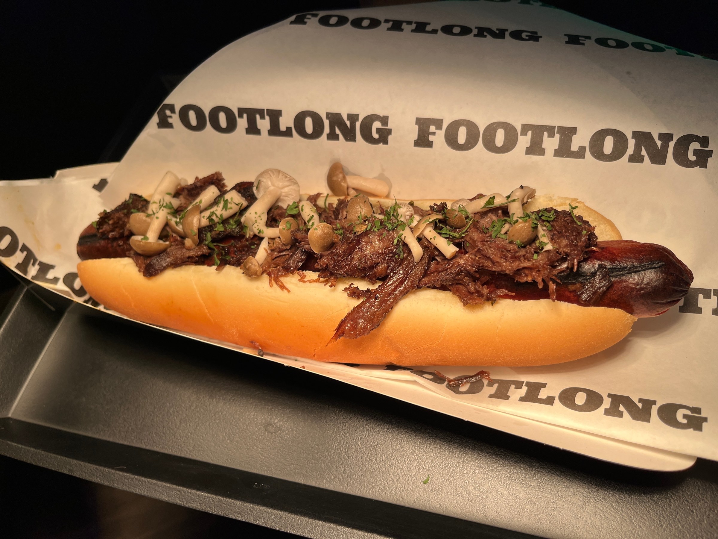 A hot dog topped with short rib and mushrooms.