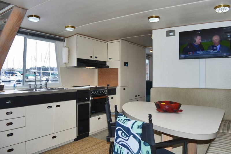 A mostly white interior of a houseboat has a football game on the TV