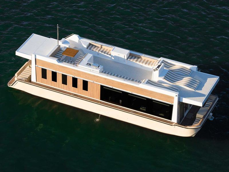 A wide, relatively flat, tan houseboat with an expansive rooftop deck.