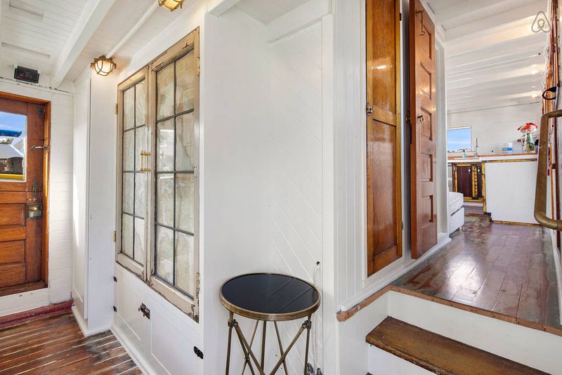 The interior of a houseboat features wooden doors. A staircase leads off to another area on the right.